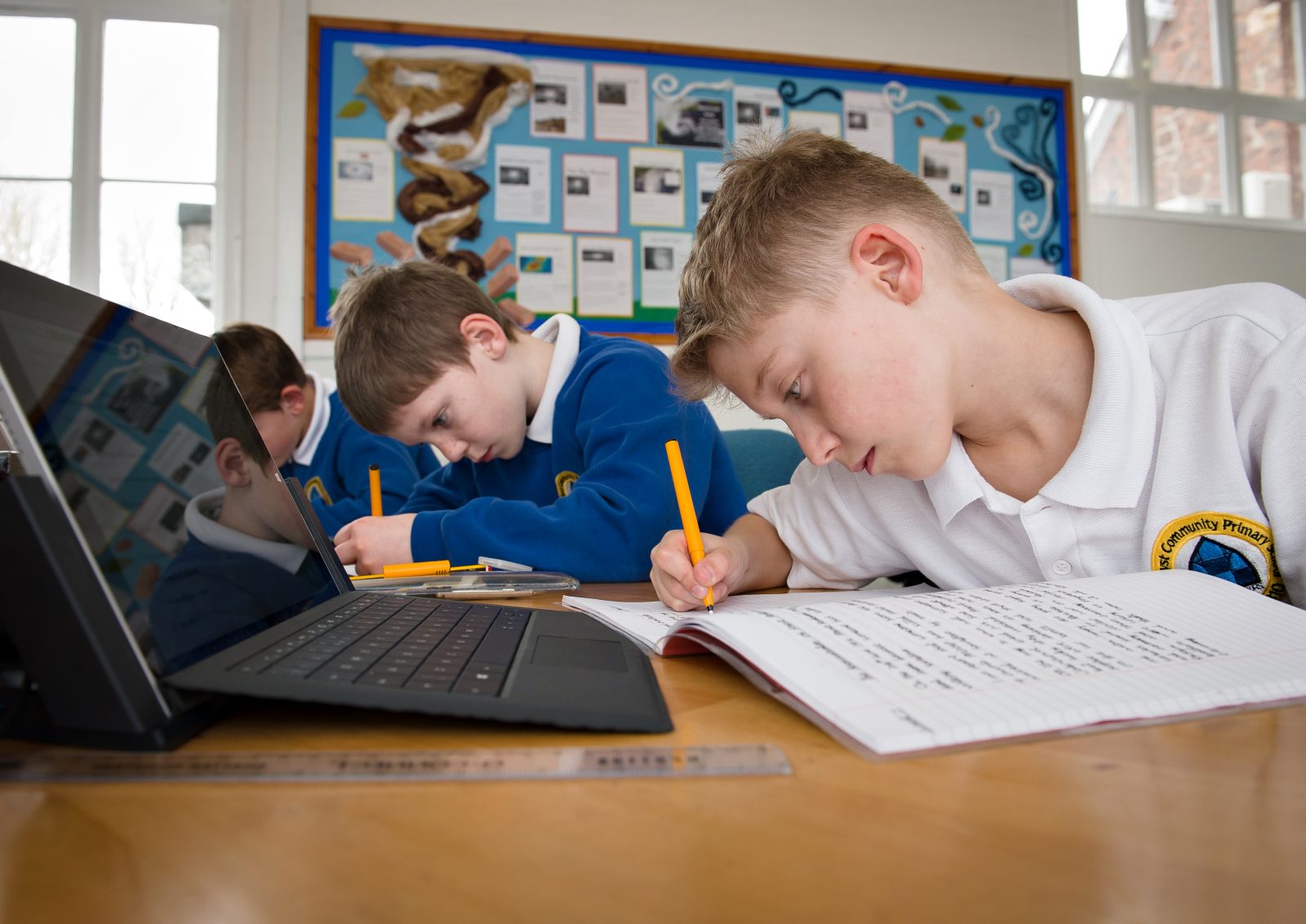 Pupils at Cornerstone Academy Trust use laptops as part of their school work. Here they are writing in their school notebooks while having laptops set out in front of them. 