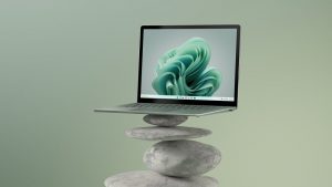 Promotional photo of a Surface Laptop 5 in Sage sitting atop stones arranged in a pile.