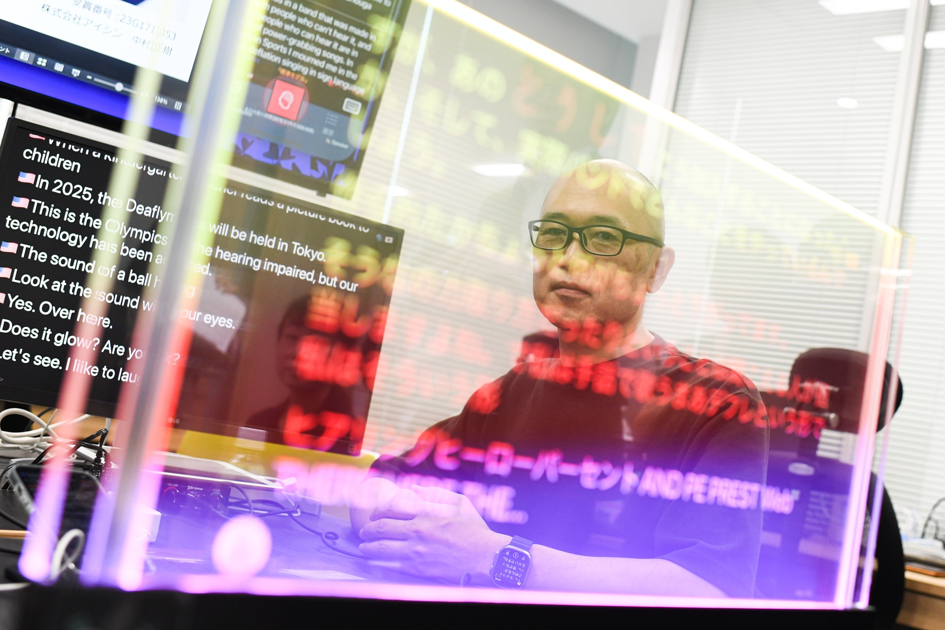 Man at a computer behind a glass screen projecting Japanese text