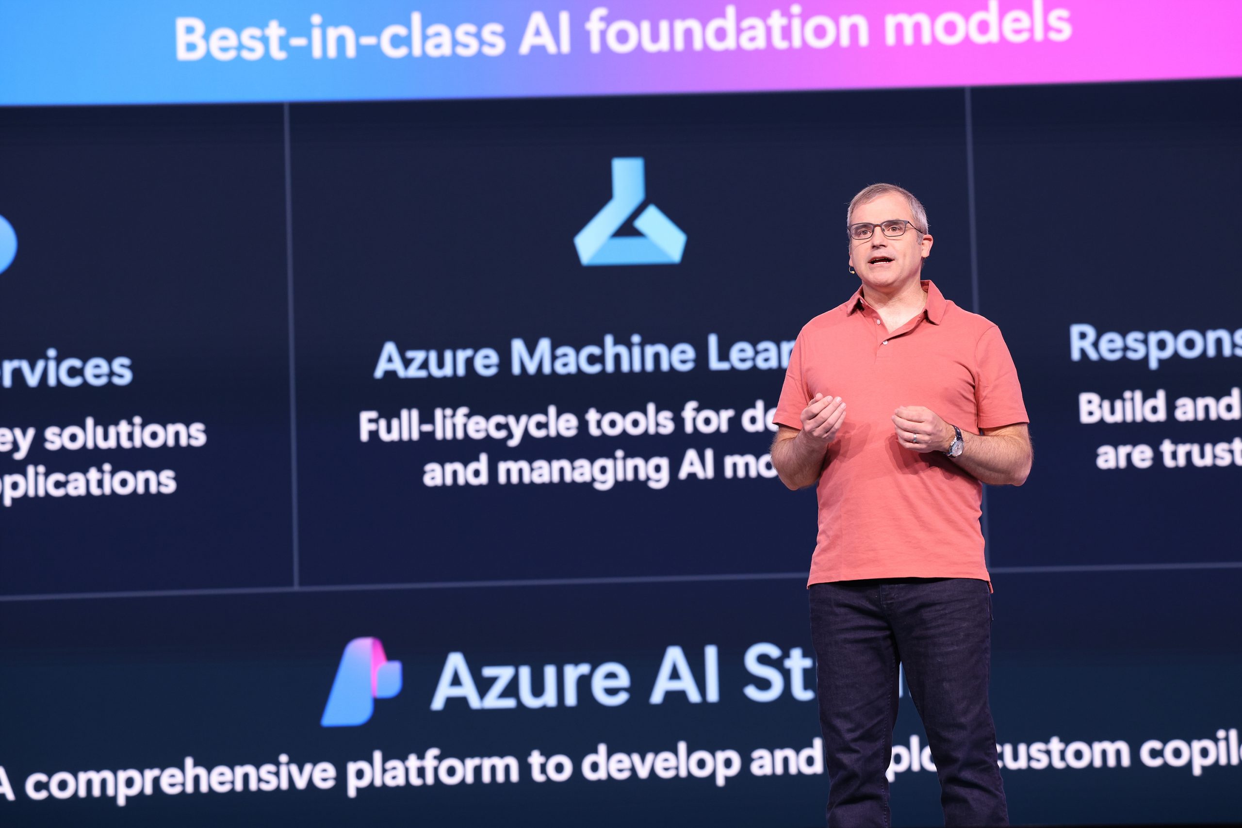 A man standing on stage speaking to an audience with text about best-in-class AI foundation models on a screen behind him