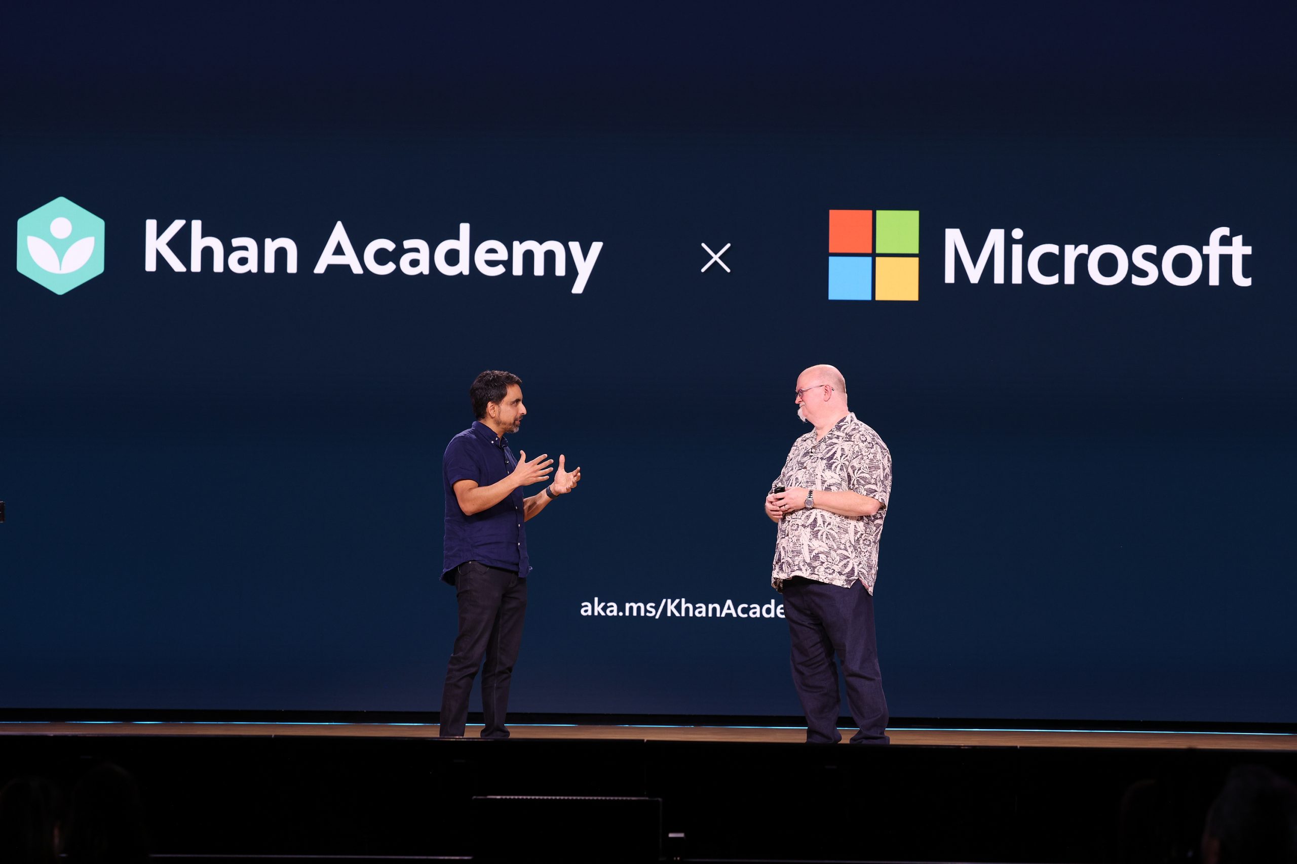Two men standing on stage with Khan Academy and Microsoft logos on a screen behind them