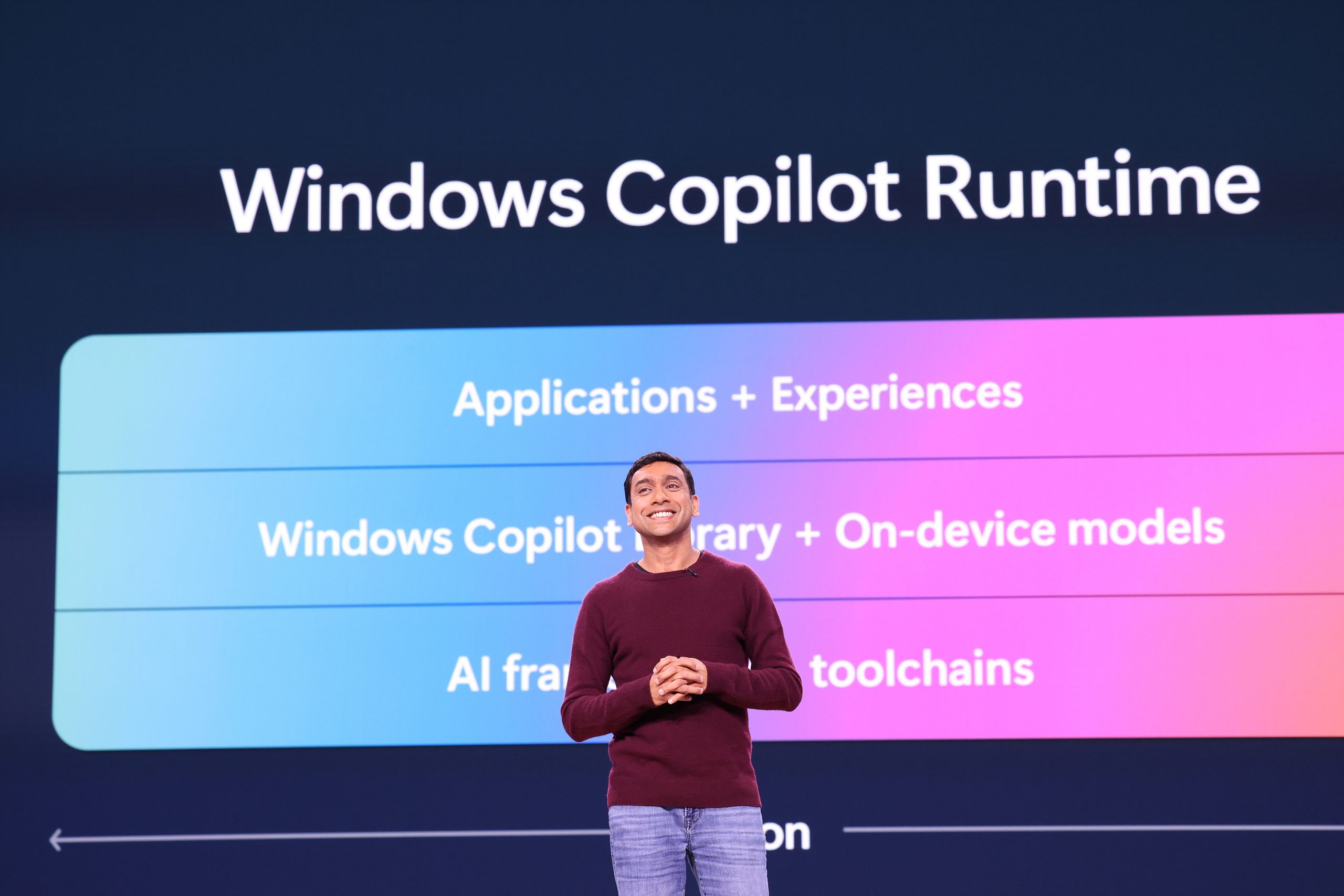 A man standing on stage, text on a screen behind him that outlines elements of Windows Copilot Runtime