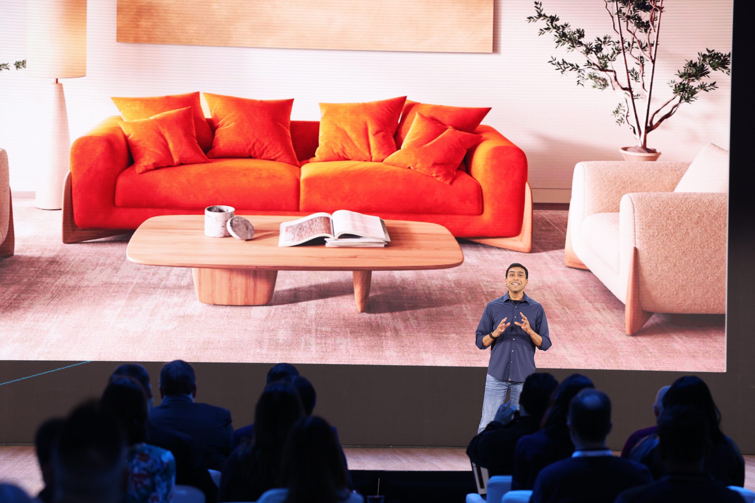 A man standing on stage in front of an audience, with an image of a living room on the screen behind him