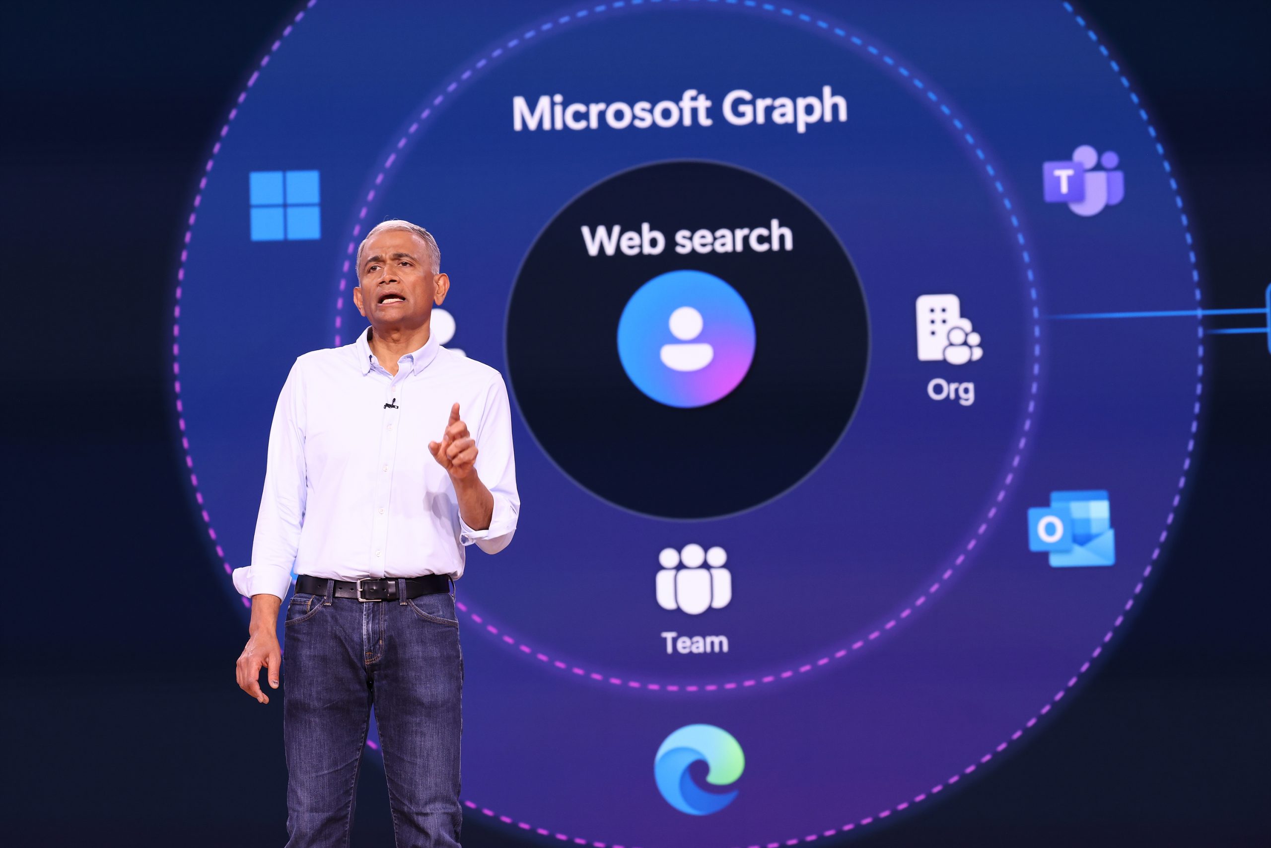 A man standing on stage with a Microsoft Graph illustration on a screen behind him