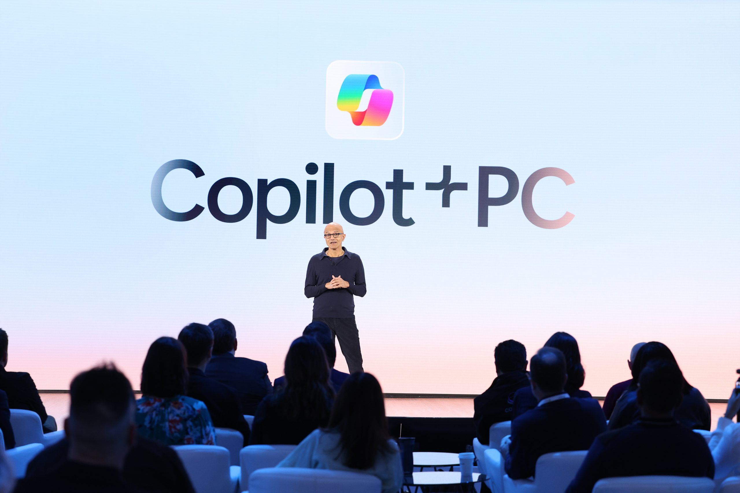 A man stands on a stage in front of an audience under the words “Copilot+ PC”