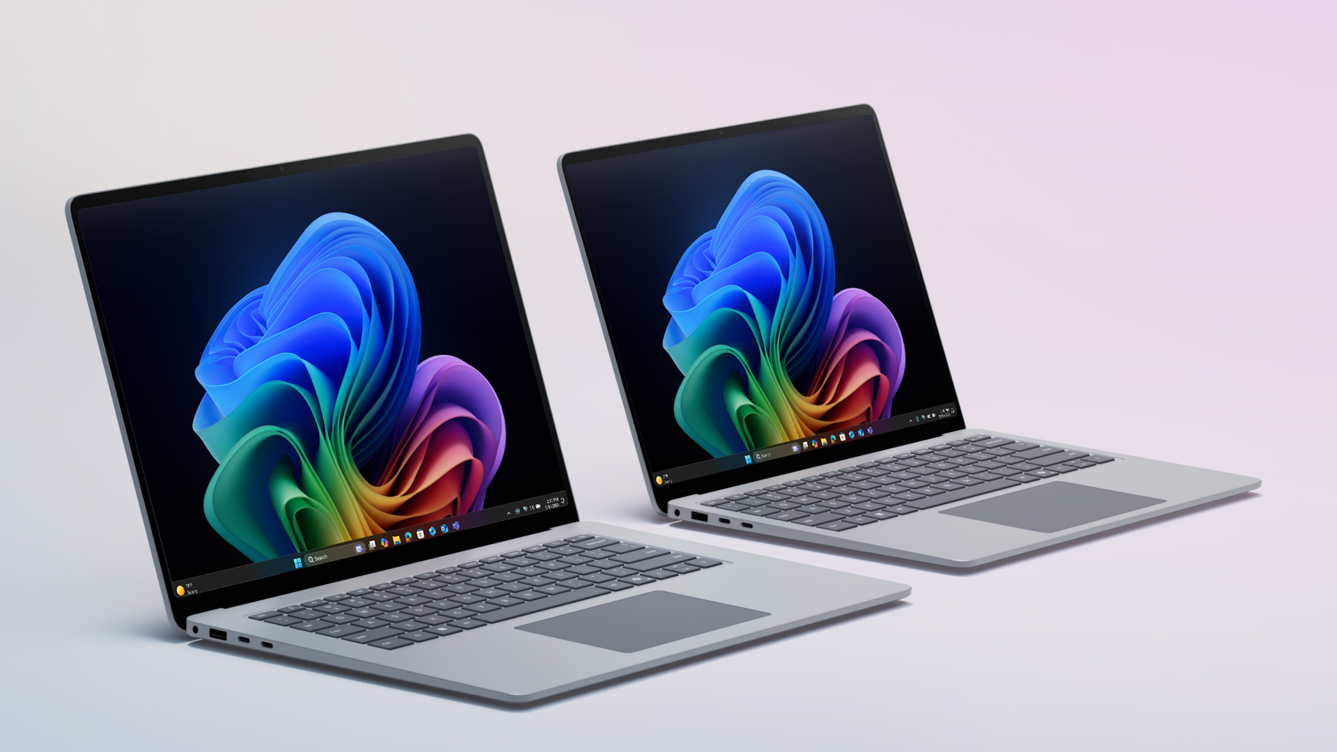 Two grey Surface Laptops for Enterprise next to each other opened with the Windows rainbow bloom image home page in dark mode.