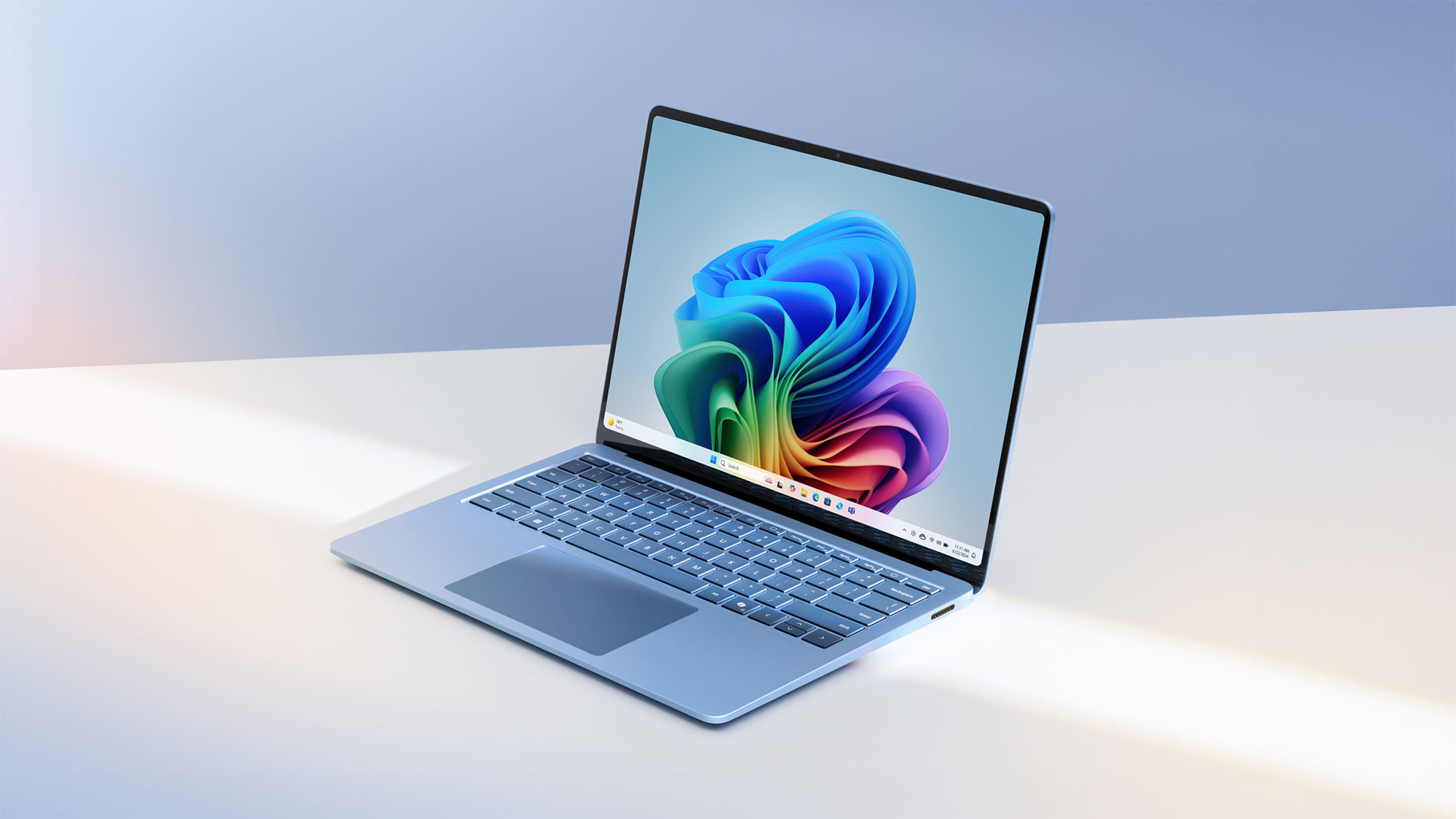 Angled front view of an open blue Surface Laptop facing the left with the Windows rainbow bloom image on the home screen.