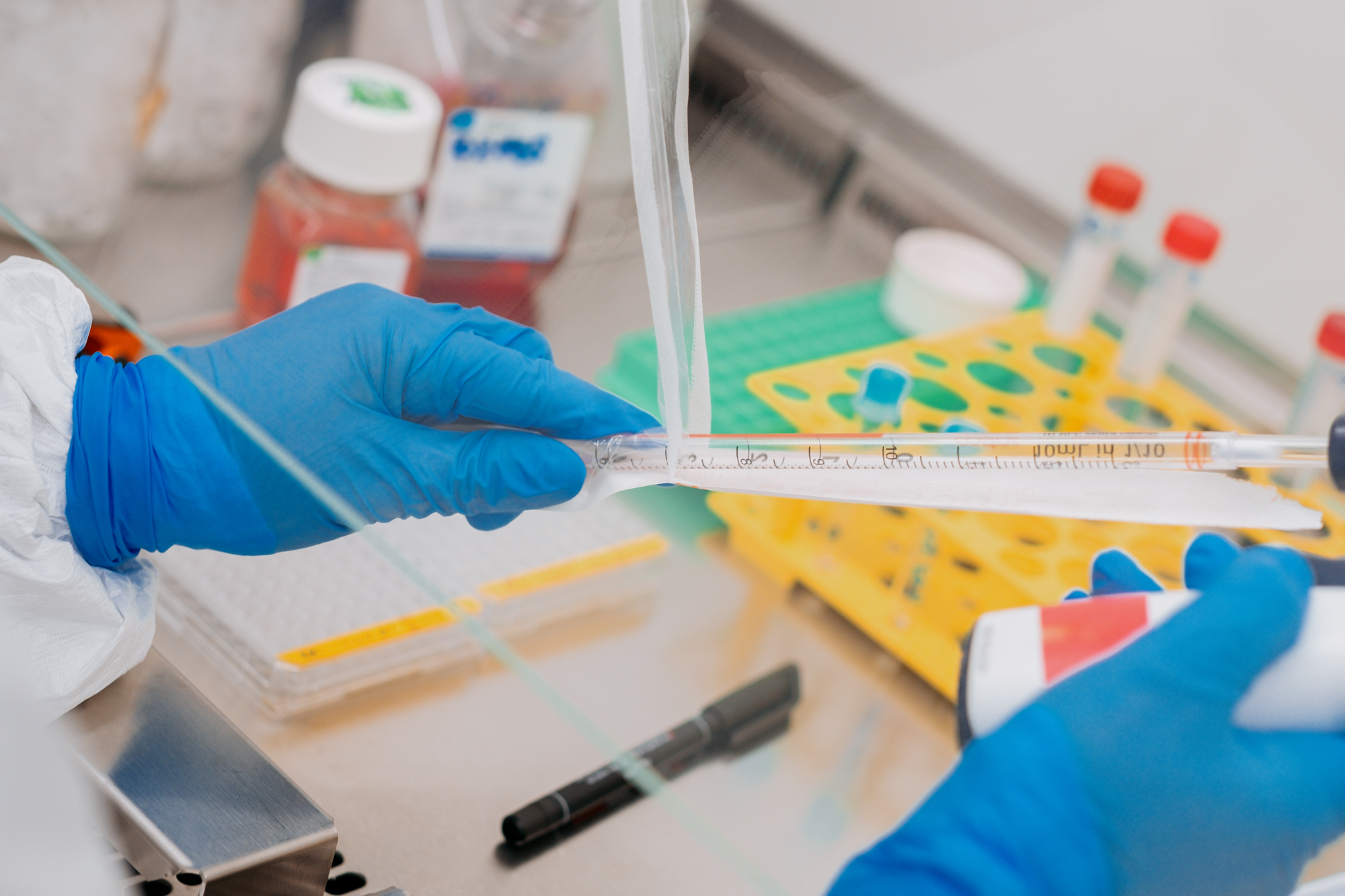 A closeup of blue-gloved hands handling a long glass tube in a lab.