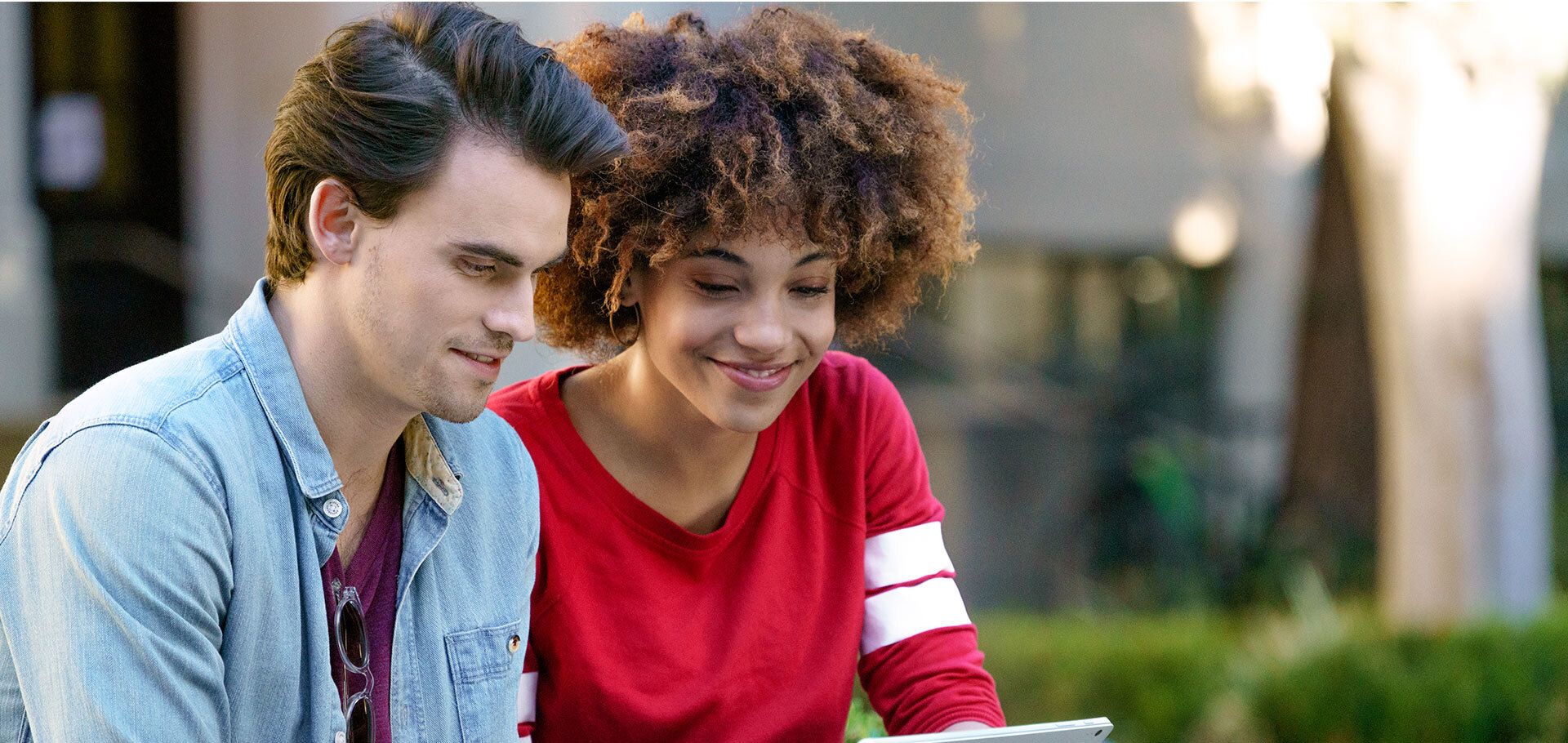 A boy in a denim shirt and a woman with curls in a red top looking at the laptop together