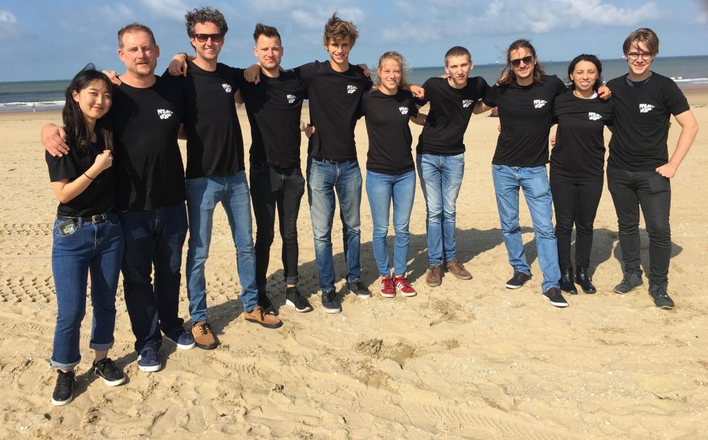 10 members of the team behind BeachBot stand in a line at the beach. 