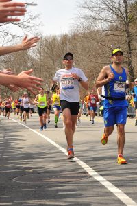 photo of runners at the Boston Marathon with hands from the crowd waving to cheer them along