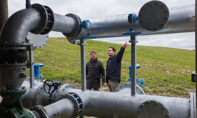 Two men look at metal water pipes in a field
