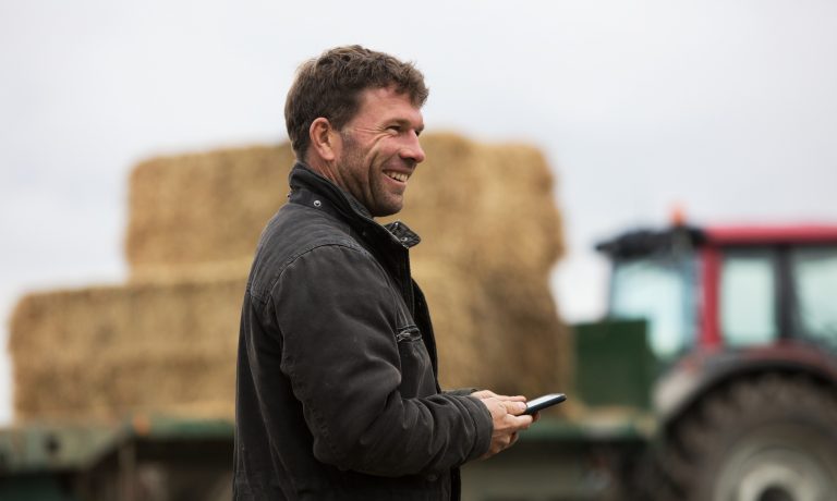 Craig Blackburn smiles while holding phone in front of farm equipment