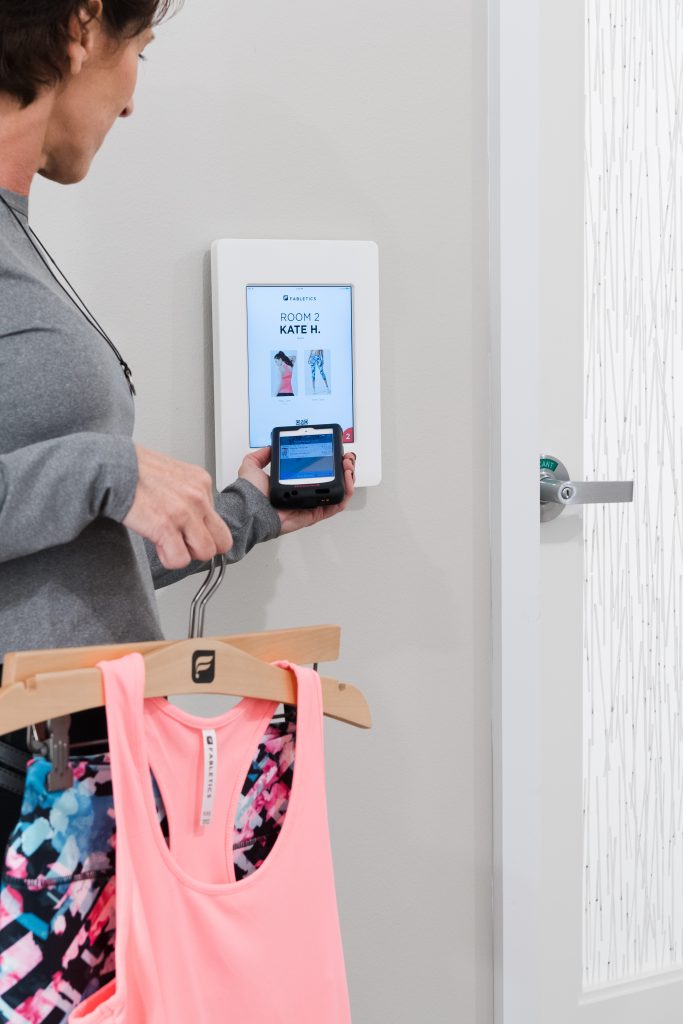 A Fabletics shopper touches her smart phone to a panel outside a fitting room.