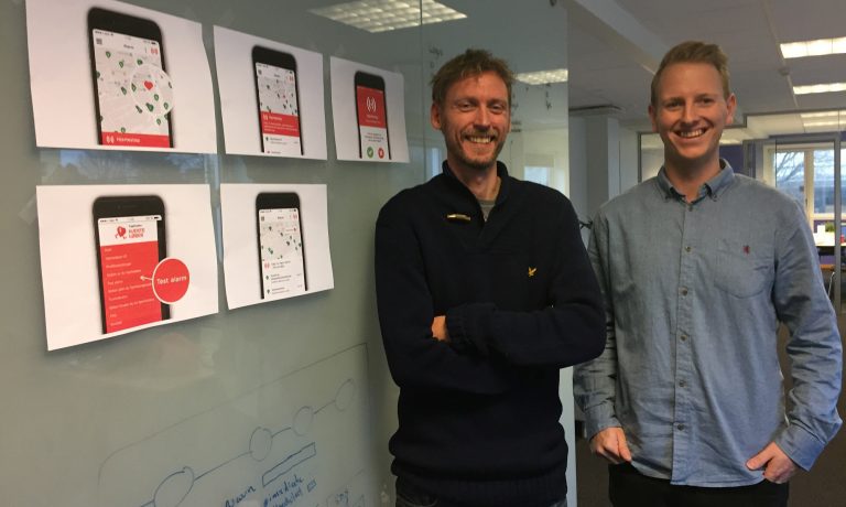 Two men smile and stand next to pictures of the Heartrunner mobile app