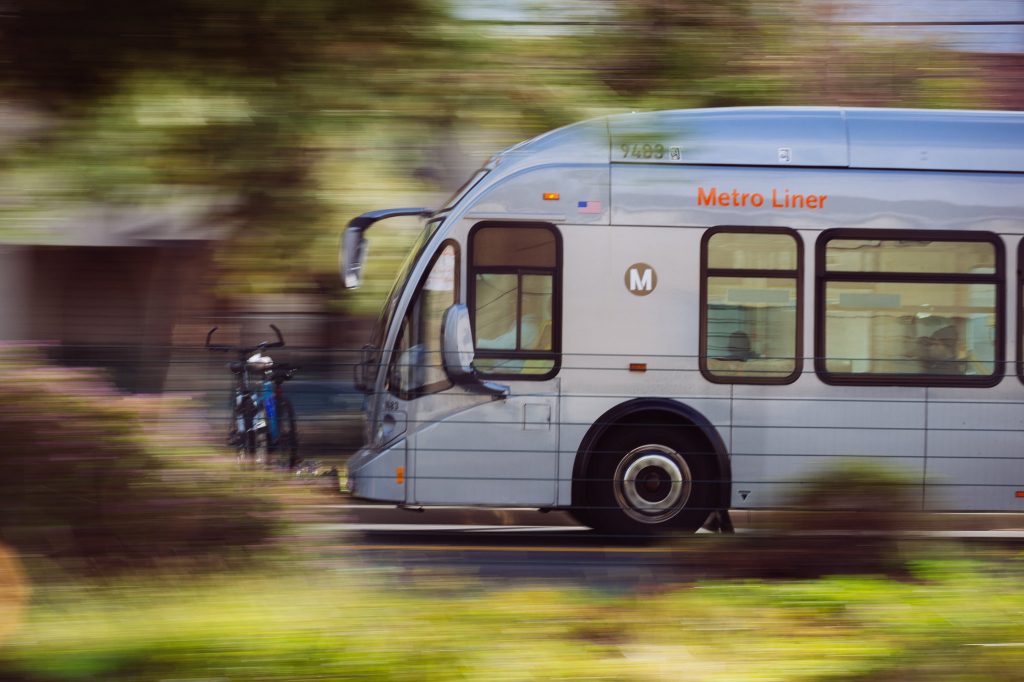 Side view of silver bus moving past greenery
